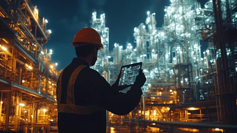 夜間の照明に照らされた工業現場で、タブレットを操作するヘルメット着用の作業員