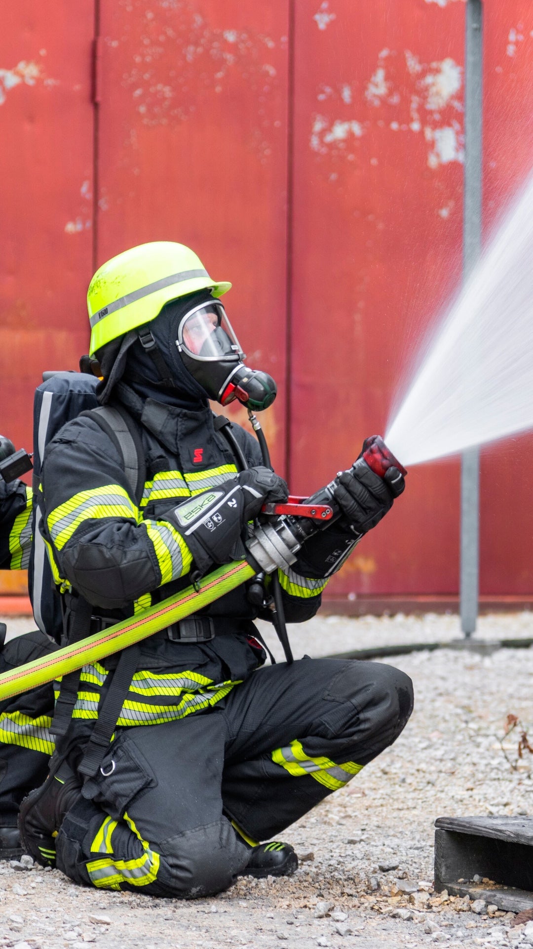 firefighter kneeling and spraying water from their hose
