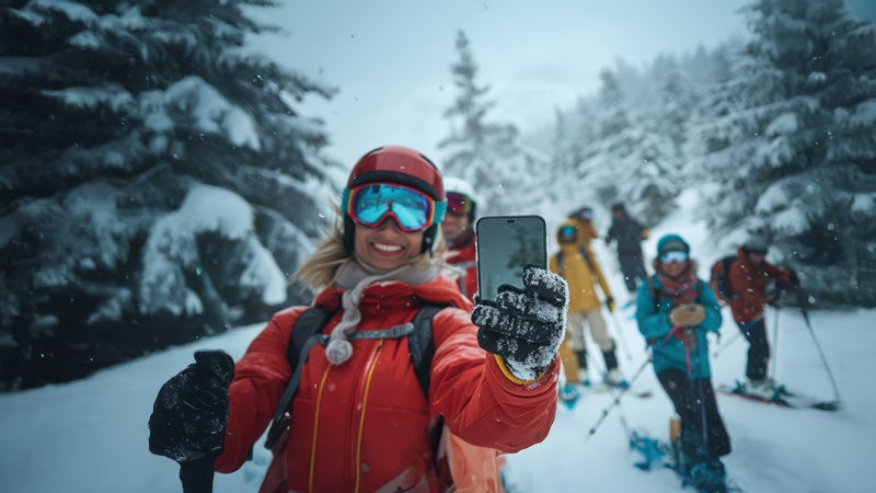 雪のトレイルを歩きながらモバイル機器を手にする女性