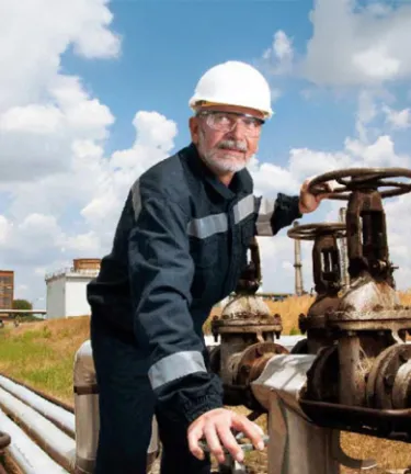 Worker fixing a long pipe on a field while wearing PPE.
