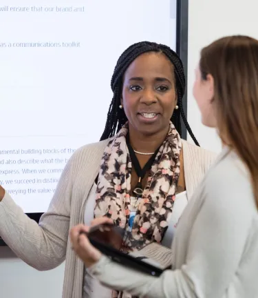two female associates speaking in a meeting room next to a whiteboard